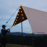 A man setting up his sunshade tarp and adding fairy lights on it as well